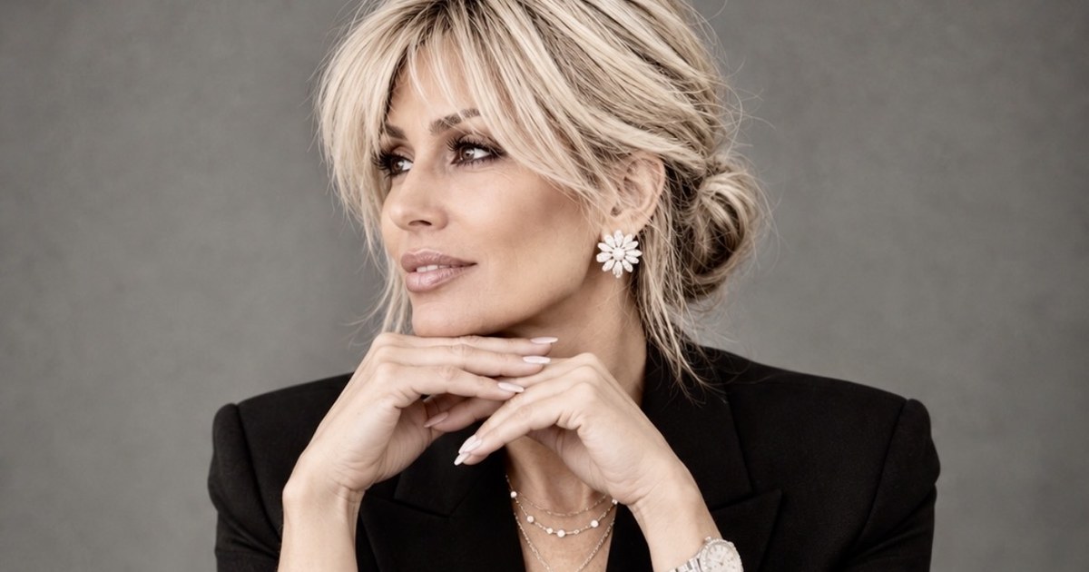 Kim Fisher in a black suit, seated with her hands folded beneath her chin, looking off camera