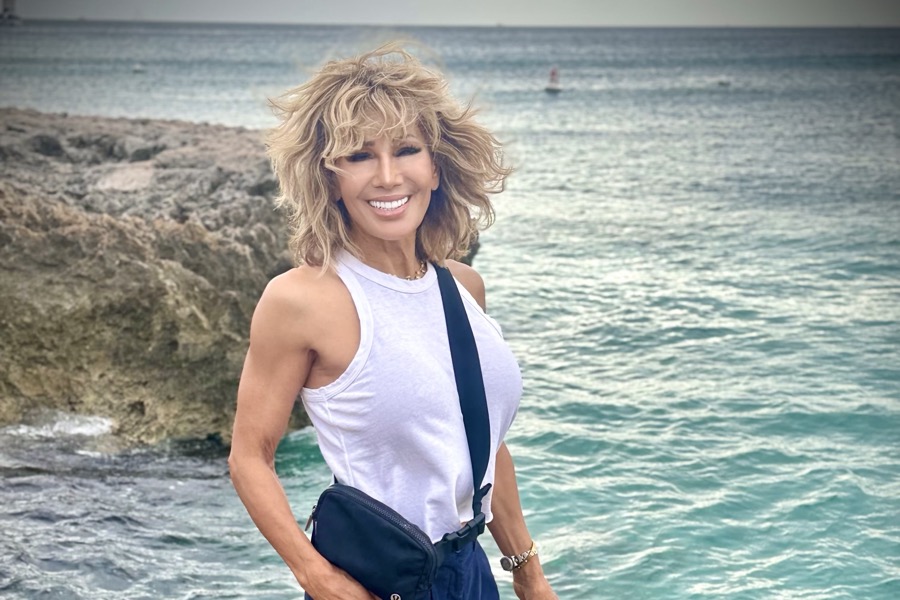 Kim Fisher on the rocks by the water in a white tank, strong and smiling